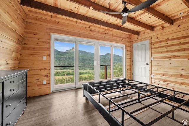 bedroom with wood walls, beamed ceiling, wooden ceiling, a mountain view, and hardwood / wood-style floors