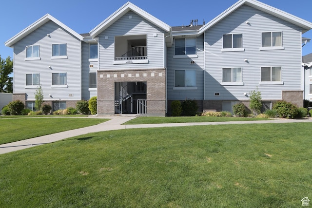 view of property featuring a front lawn, brick siding, and a balcony