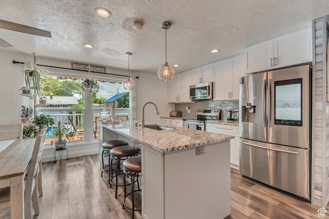 kitchen with appliances with stainless steel finishes, a sink, wood finished floors, white cabinetry, and a textured ceiling