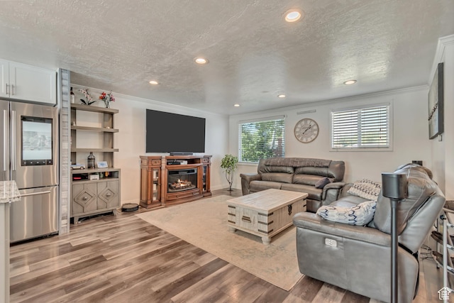 living area featuring crown molding, light wood finished floors, a glass covered fireplace, a textured ceiling, and recessed lighting