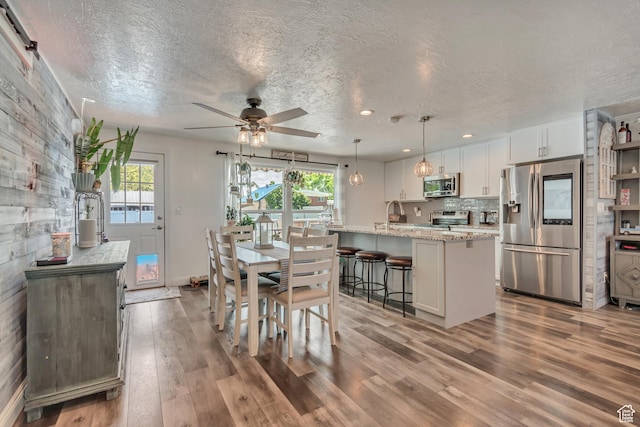 dining space with a ceiling fan, wood finished floors, a textured ceiling, baseboards, and recessed lighting