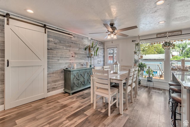 dining space featuring a barn door, a ceiling fan, baseboards, wood finished floors, and a textured ceiling