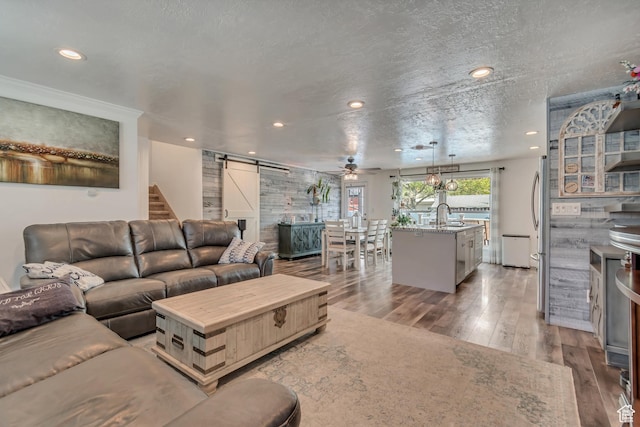 living room featuring a barn door, light wood-style flooring, recessed lighting, ceiling fan, and a textured ceiling