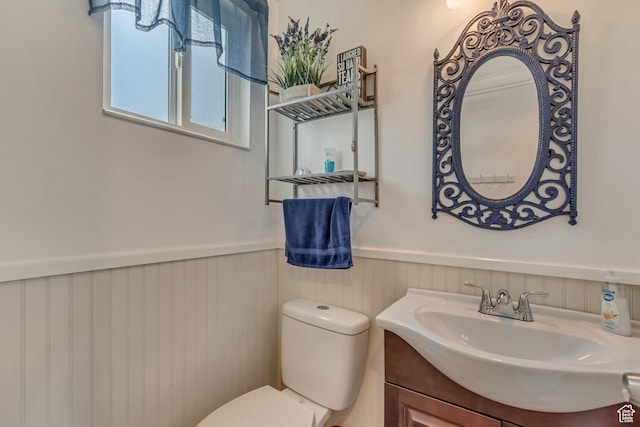 half bathroom with a wainscoted wall, toilet, and vanity