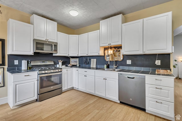 21 E Angelo Ave S, South Salt Lake, UT 84115 - kitchen featuring stainless steel appliances, light wood finished floors, a sink, and white cabinetry