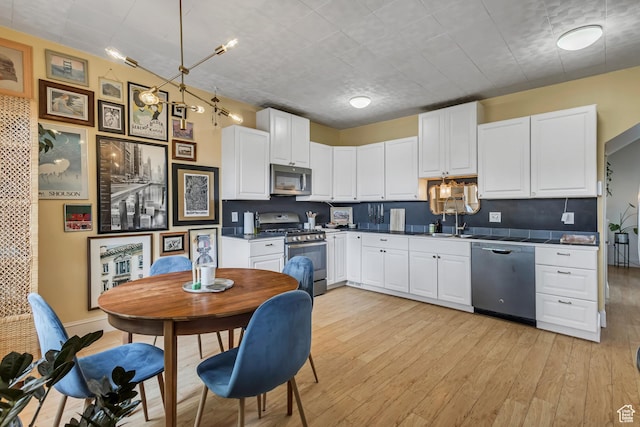 21 E Angelo Ave S, South Salt Lake, UT 84115 - kitchen featuring stainless steel appliances, white cabinets, light wood-style floors, dark countertops, and a sink