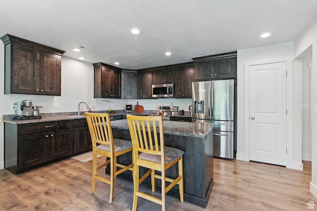 kitchen featuring stainless steel appliances, light wood-type flooring, a kitchen bar, a center island, and recessed lighting