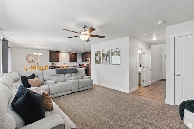 living room featuring light carpet, ceiling fan, a chandelier, and baseboards
