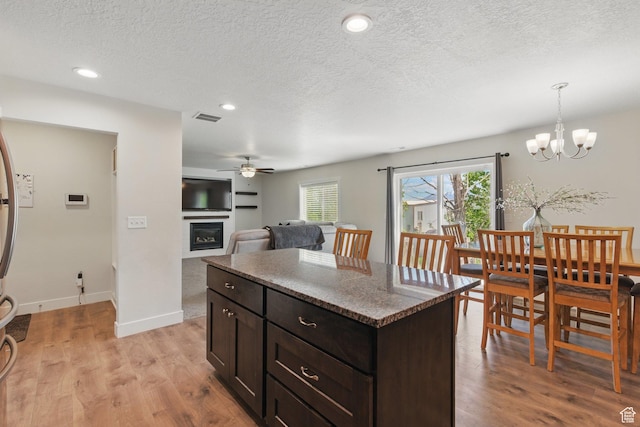 kitchen with ceiling fan, light wood-style floors, a glass covered fireplace, a textured ceiling, and a kitchen island