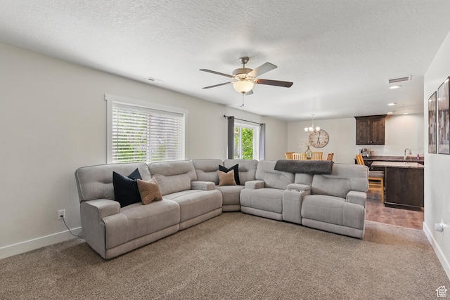 carpeted living room featuring a chandelier, a ceiling fan, a sink, baseboards, and a textured ceiling