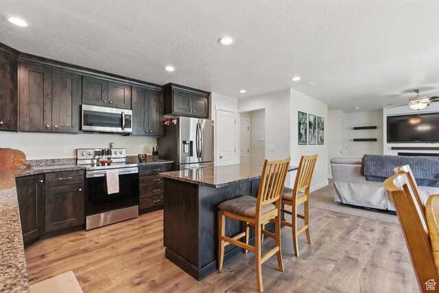 kitchen featuring stainless steel appliances, a breakfast bar area, dark stone countertops, light wood finished floors, and recessed lighting