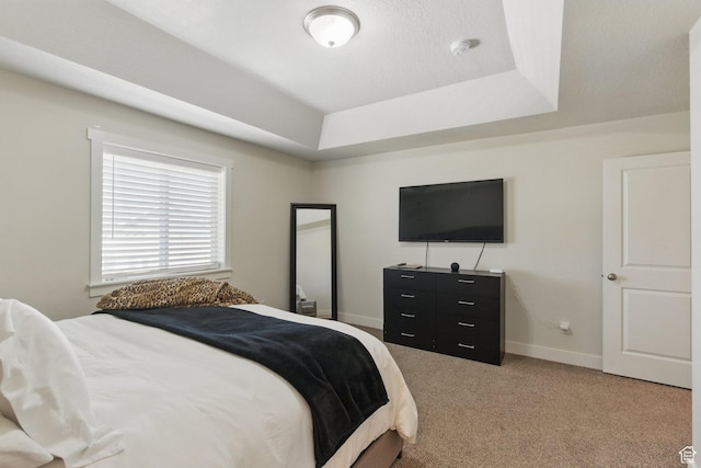 bedroom featuring light colored carpet, a raised ceiling, and baseboards