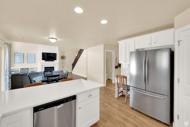 kitchen featuring appliances with stainless steel finishes, light wood-style flooring, light countertops, white cabinetry, and a fireplace