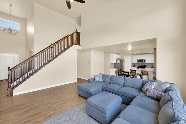 living room featuring a high ceiling, stairs, light wood-type flooring, ceiling fan, and baseboards