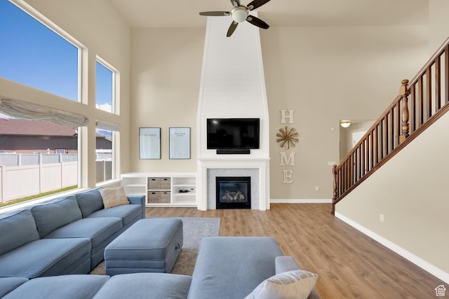 living room with a towering ceiling, a ceiling fan, stairs, light wood-type flooring, and baseboards