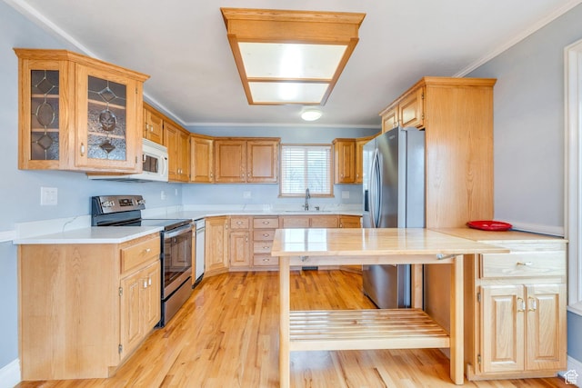 kitchen with appliances with stainless steel finishes, a sink, light countertops, glass insert cabinets, and light wood finished floors