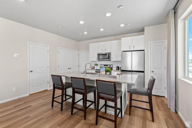 351 N Riverside Dr Unit 978, Saratoga Springs, UT 84045 - kitchen with stainless steel appliances, a sink, light wood-style floors, an island with sink, and white cabinetry