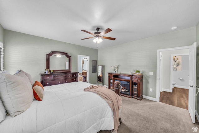 carpeted bedroom with connected bathroom, baseboards, a ceiling fan, and a warm lit fireplace
