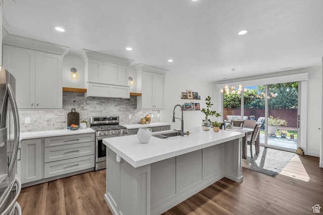 kitchen with stainless steel appliances, a sink, light countertops, decorative backsplash, and a kitchen island with sink