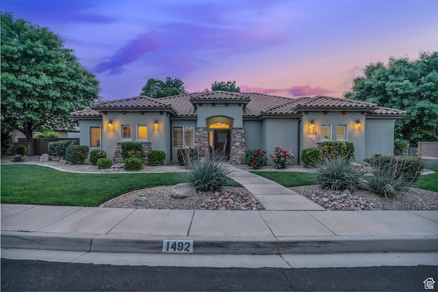 mediterranean / spanish home featuring stucco siding, a yard, and a tiled roof