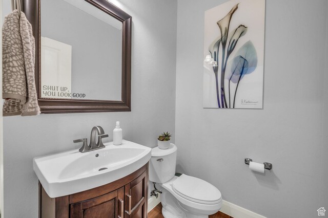 half bathroom featuring toilet, baseboards, and vanity