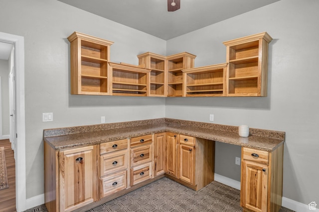 unfurnished office with built in study area, dark floors, baseboards, and a ceiling fan