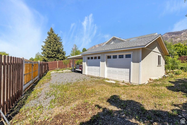 view of side of home with a fenced backyard, a garage, and roof with shingles