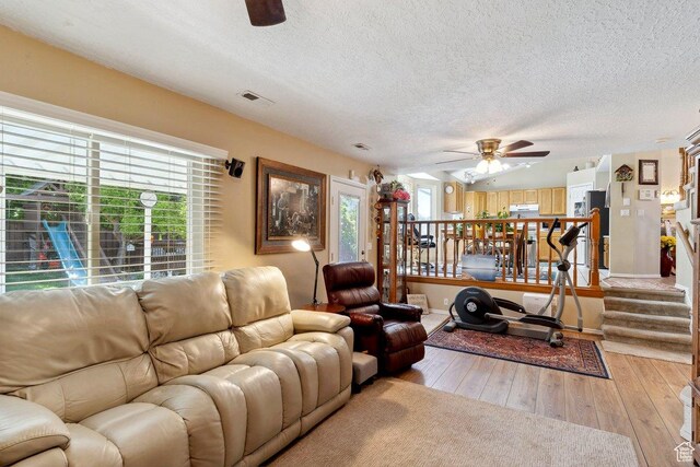 living area with ceiling fan, healthy amount of natural light, a textured ceiling, light wood finished floors, and baseboards