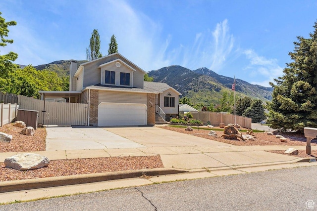 view of front of home with driveway, an attached garage, a mountain view, brick siding, and fence