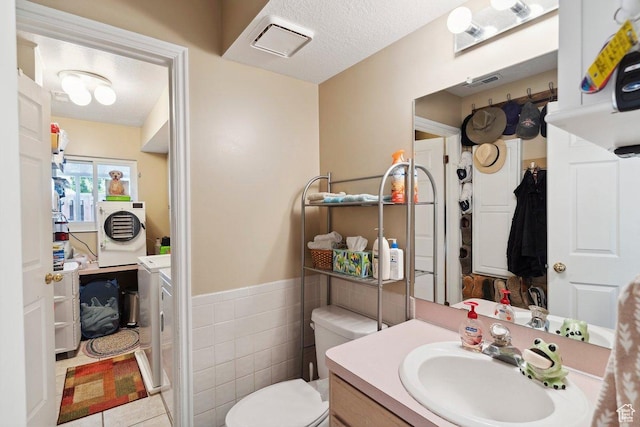 bathroom with washer and dryer, toilet, tile patterned flooring, vanity, and a wainscoted wall