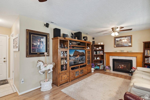 living area with a ceiling fan, wood finished floors, a fireplace, a textured ceiling, and baseboards