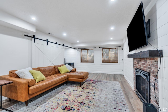 living area with a barn door, light wood-style flooring, recessed lighting, and a brick fireplace