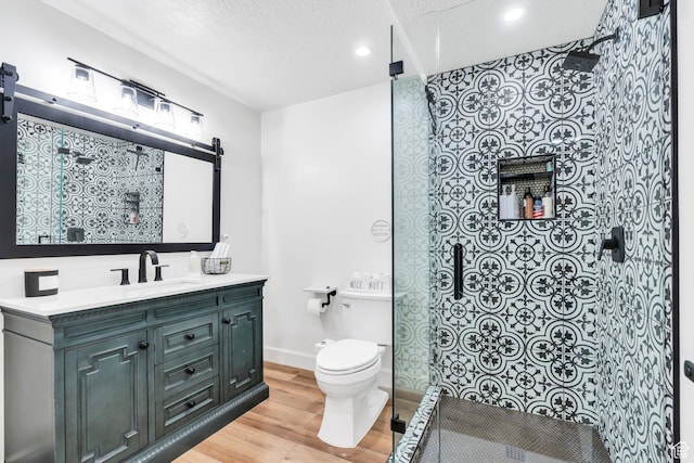 bathroom with wood finished floors, a walk in shower, toilet, vanity, and recessed lighting