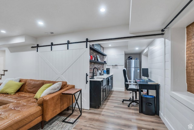 office featuring light wood-style flooring, a barn door, recessed lighting, and a sink