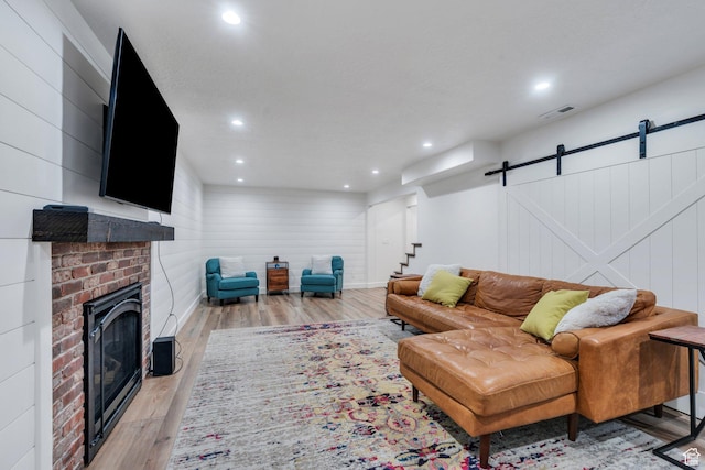 living area with a barn door, light wood-style floors, a brick fireplace, recessed lighting, and stairway