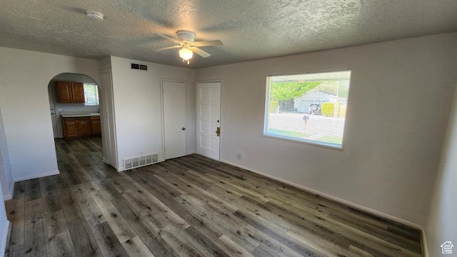 empty room with arched walkways, a ceiling fan, dark wood finished floors, a textured ceiling, and a smoke detector