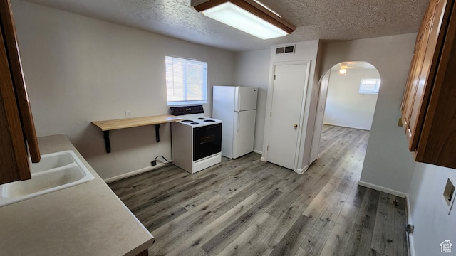 kitchen with electric range oven, freestanding refrigerator, arched walkways, plenty of natural light, and a textured ceiling