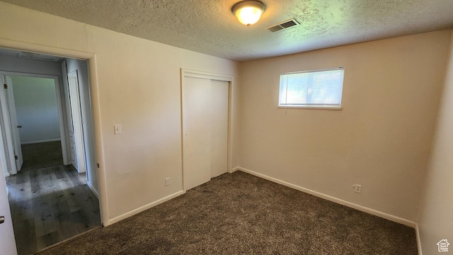 unfurnished bedroom with a textured ceiling, a closet, baseboards, and dark carpet