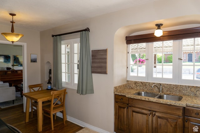 kitchen with a sink, arched walkways, dark wood finished floors, baseboards, and light stone countertops