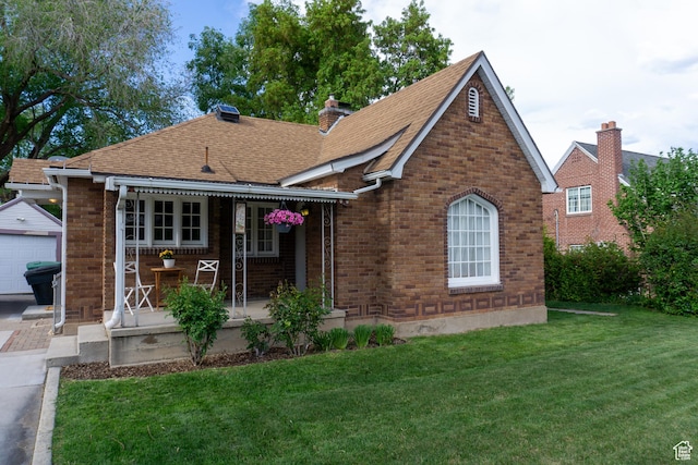 tudor house with a front yard, an outbuilding, a shingled roof, and brick siding
