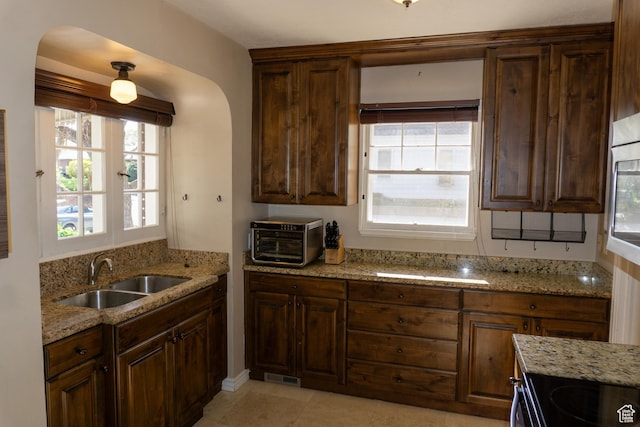 kitchen featuring a sink, light stone countertops, arched walkways, black electric range oven, and light tile patterned floors