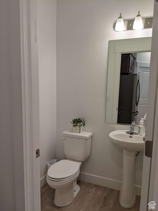 bathroom featuring wood finished floors, baseboards, toilet, and a sink