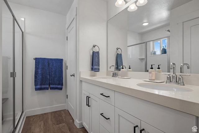 bathroom featuring a stall shower, wood finished floors, double vanity, and baseboards