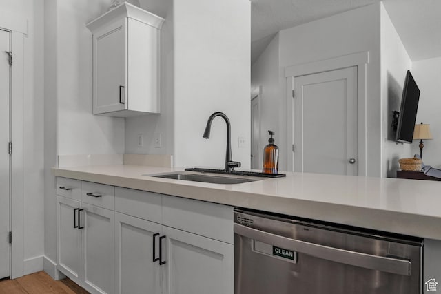 kitchen with dishwasher, a sink, white cabinets, light wood-style flooring, and light countertops