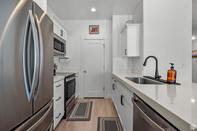 kitchen featuring stainless steel appliances, a sink, white cabinetry, light wood-type flooring, and recessed lighting