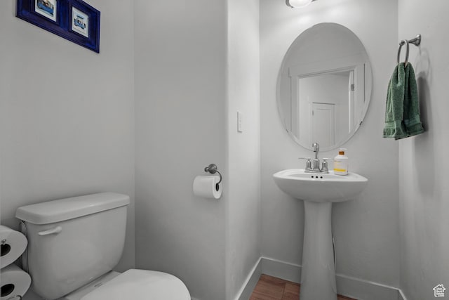 half bath featuring toilet, wood finished floors, and baseboards