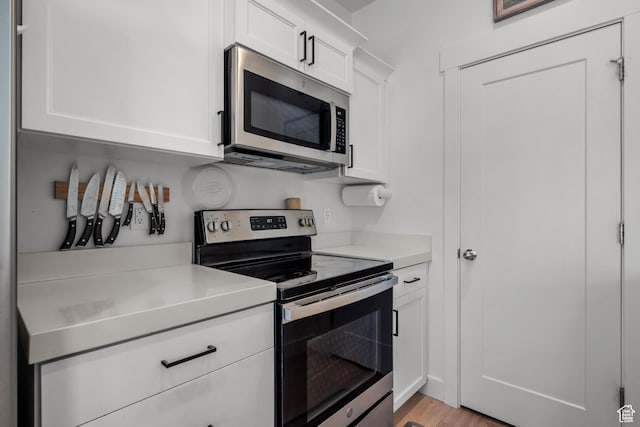 kitchen with stainless steel appliances, light countertops, white cabinets, and light wood-style flooring