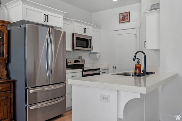 kitchen featuring stainless steel appliances, a sink, white cabinets, a peninsula, and light countertops