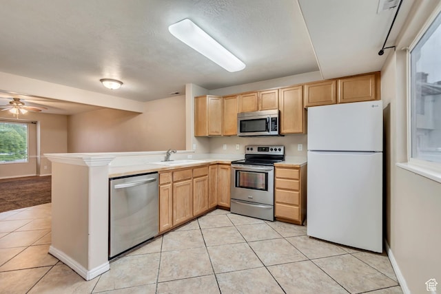 kitchen with appliances with stainless steel finishes, a sink, light brown cabinets, light tile patterned floors, and a peninsula