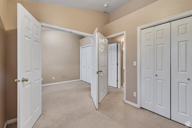 unfurnished bedroom featuring light colored carpet, two closets, and baseboards